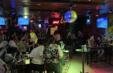 Interior shot of Badlands Las Vegas, a popular gay bar. People are socializing, with a disco ball and neon signs enhancing the atmosphere.