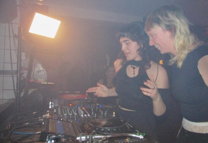 Baggen Copenhagen: Two women DJs at a gay club, smiling and working the turntables. Nightlife scene, music, and travel advice.