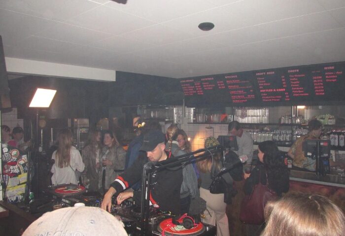 Baggen Copenhagen: Gay bar scene with DJ playing music for a crowd. Menu board visible. Gay travel advice.