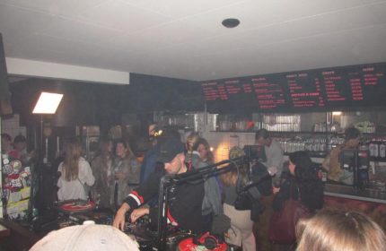 Baggen Copenhagen: Gay bar scene with DJ playing music for a crowd. Menu board visible. Gay travel advice.
