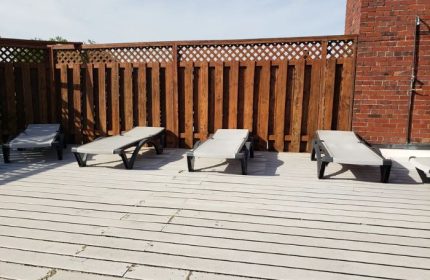 Bain Colonial Bath, a gay spa in Montreal: Lounge chairs on a wooden deck with a fence and brick wall. Perfect for relaxation.