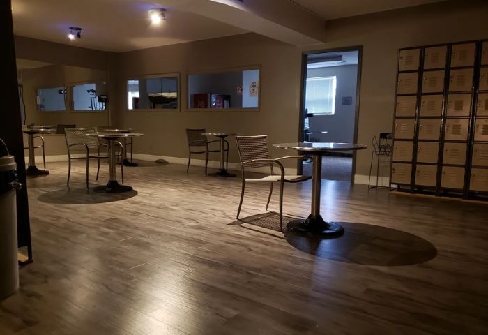 Lounge area at Bain Colonial, a gay bathhouse and spa in Montreal. Tables, chairs, lockers, and mirrors are visible.