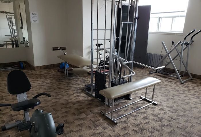 Bain Colonial gay spa in Montreal gym. Exercise equipment includes bike, weight machine, bench, and elliptical. Gay travel advice.
