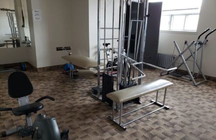 Bain Colonial gay spa in Montreal gym. Exercise equipment includes bike, weight machine, bench, and elliptical. Gay travel advice.