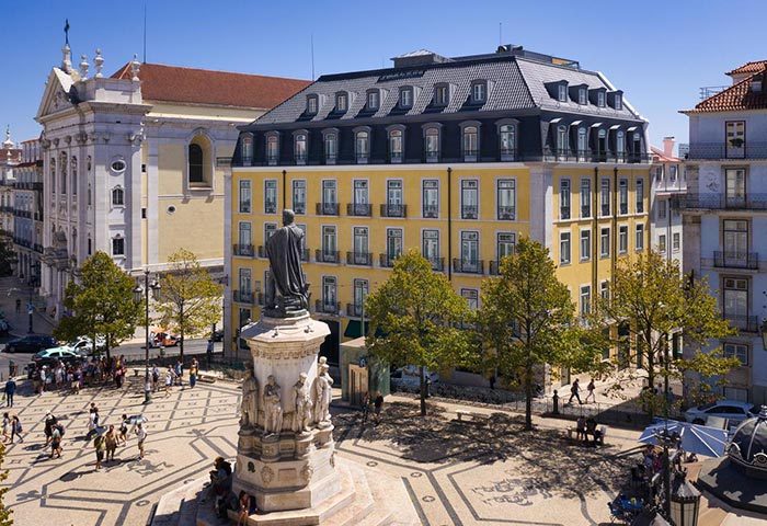 Bairro Alto Hotel, Lisbon. Luxury gay hotel in main tourist area. Yellow building with statue in foreground and people walking around.