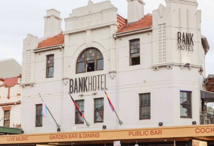 Bank Hotel, Newtown: White building with BANK HOTEL signage. Flags fly below, advertising live music, garden bar, and public bar. Gay travel.