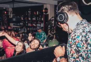 Gay nightlife at Newtown's Bank Hotel: DJ with headphones plays music for a happy crowd at the bar. Gay travel advice.