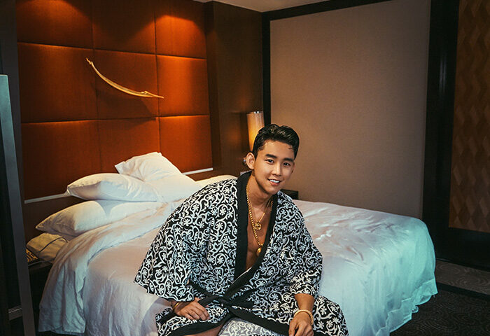 Gay Korean traveler at Banyan Tree Bangkok, a popular gay hotel. Man in robe sits on bed. Gay travel in Thailand.