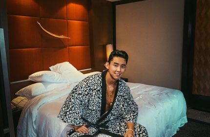 Gay Korean traveler at Banyan Tree Bangkok, a popular gay hotel. Man in robe sits on bed. Gay travel in Thailand.
