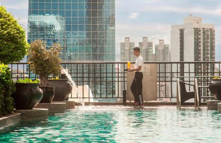 Banyan Tree Bangkok rooftop pool view. Staff carrying drinks. Top gay hotels in Bangkok for gay men, luxury travel and rooftop bars.