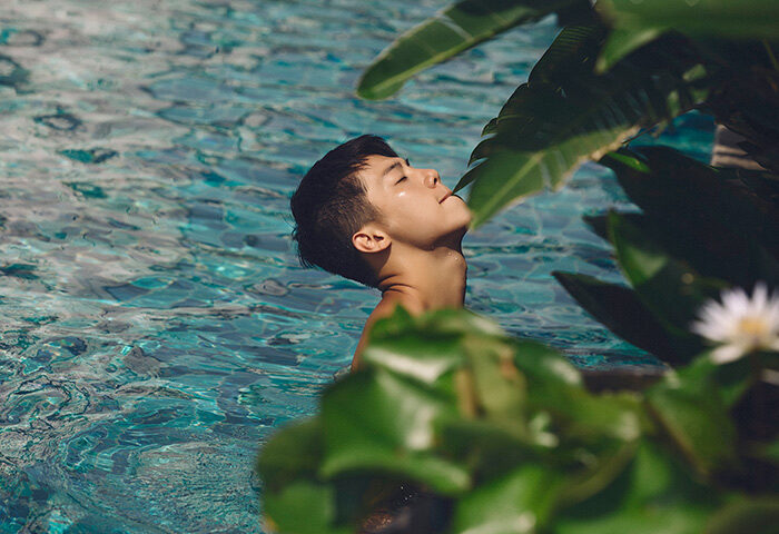 Gay man relaxes in Banyan Tree Bangkok rooftop pool. Top gay hotels on TikTok. Lush greenery, serene water.