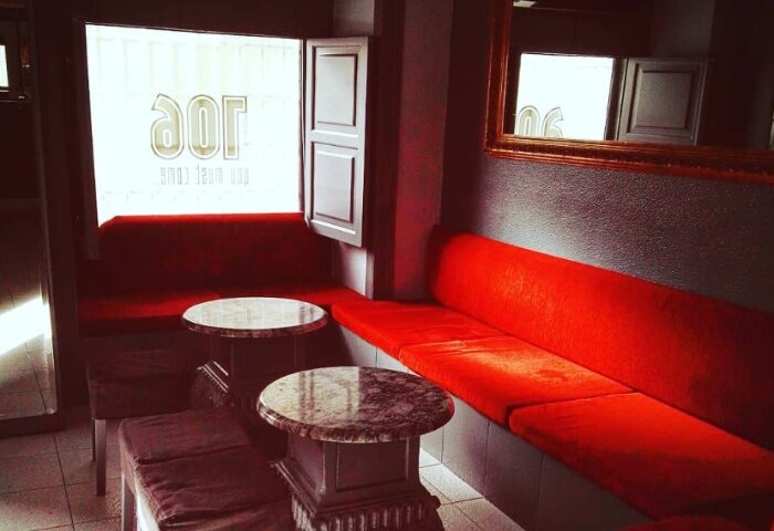 Lisbon gay bar interior. Red cushioned seating, marble tables, and a window with Joe signage. Travel advice for gay men in Lisbon.