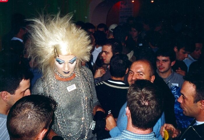 Lisbon gay bar scene: Drag queen with blonde wig and heavy makeup in a crowded club. Gay travel advice, nightlife.