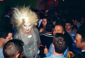 Lisbon gay bar scene: Drag queen with blonde wig and heavy makeup in a crowded club. Gay travel advice, nightlife.