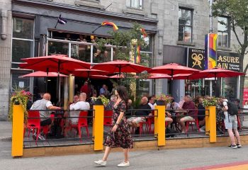 Montreal's Bar Aigle Noir: A popular gay bar with outdoor seating under red umbrellas. People enjoy drinks at this lively party spot.