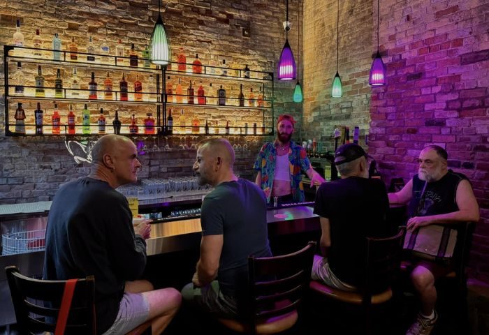 Montreal's Bar Aigle Noir: A gay bar scene with men enjoying drinks. Colorful lights, brick walls, and a well-stocked bar create a vibrant atmosphere.