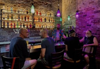 Montreal's Bar Aigle Noir: A gay bar scene with men enjoying drinks. Colorful lights, brick walls, and a well-stocked bar create a vibrant atmosphere.