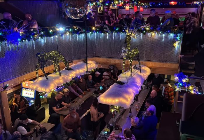 Gay bar Aigle Noir party in Montreal. Men drinking at a festive two-story bar with holiday decor and a disco ball. Nightlife scene.