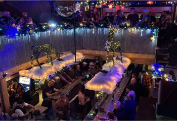 Gay bar Aigle Noir party in Montreal. Men drinking at a festive two-story bar with holiday decor and a disco ball. Nightlife scene.