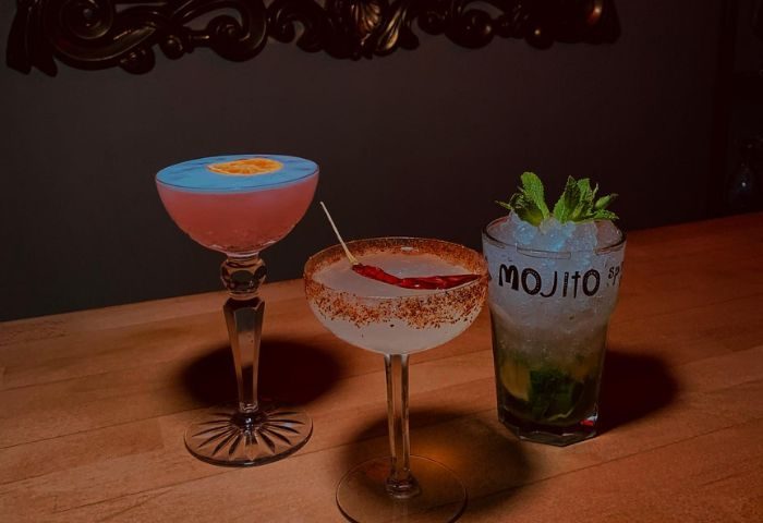 Cocktails at a Sitges gay bar. Three drinks: a blue & pink cocktail, a chili cocktail, and a mojito with mint on a wooden bar.