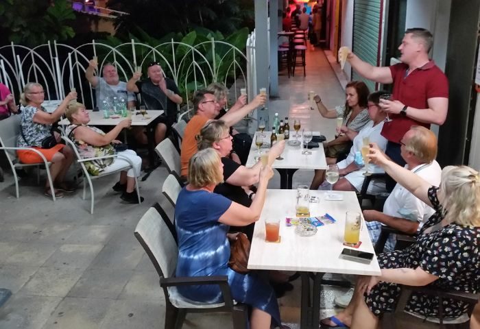 Gay bar Babel in Torremolinos, Spain. People toasting drinks at an outdoor table. Gay travel advice for men.