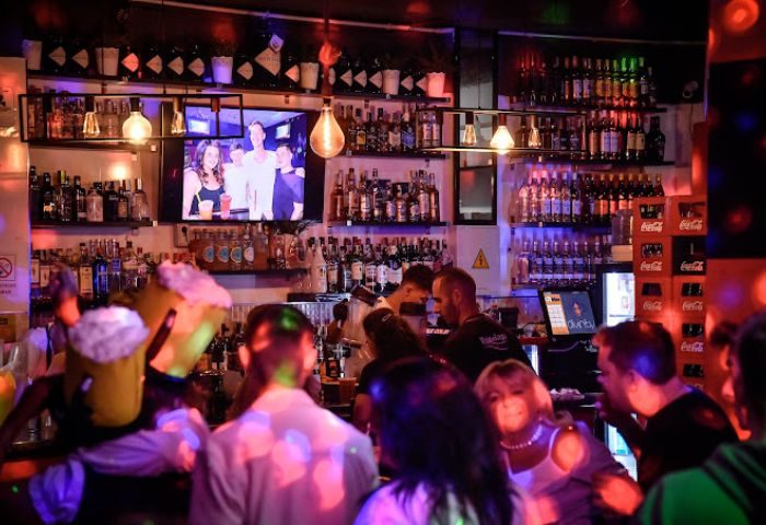 Divinity Gay Bar in Gran Canaria. Interior shot of a busy bar with people, alcohol bottles, and a TV screen. Gay travel advice.