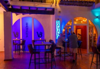 Havana Bar, a gay bar in Torremolinos, Spain. Tables and chairs are set outside with blue neon lights. People are enjoying drinks.