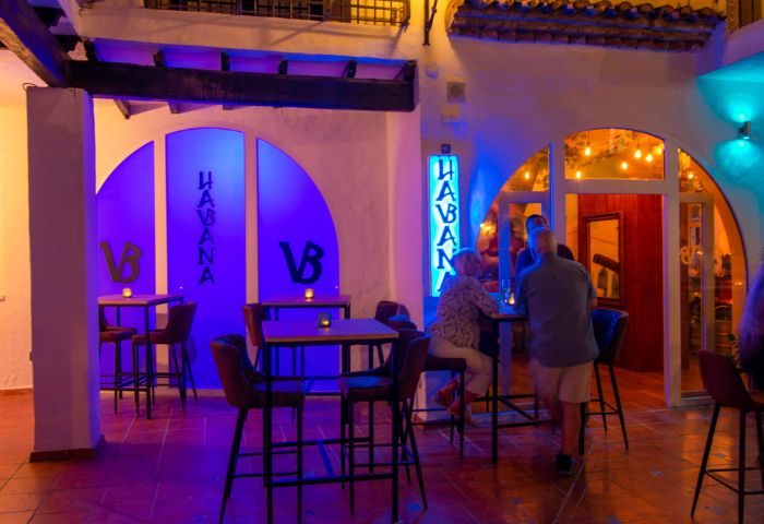 Havana Bar, a gay bar in Torremolinos, Spain. Tables and chairs are set outside with blue neon lights. People are enjoying drinks.