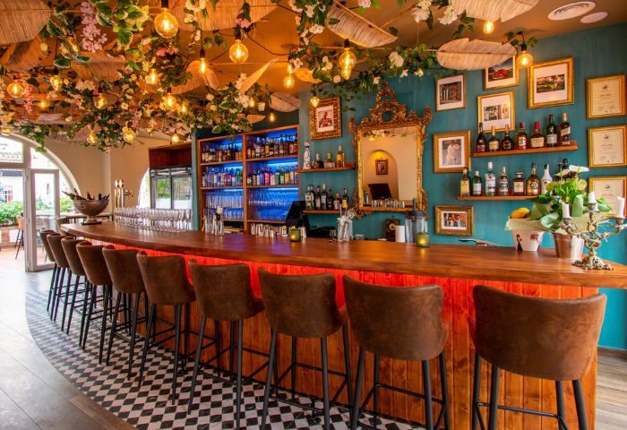 Havana gay bar in Torremolinos. Stylish interior with a long wooden bar, high stools, shelves of drinks, and floral decorations on the ceiling.