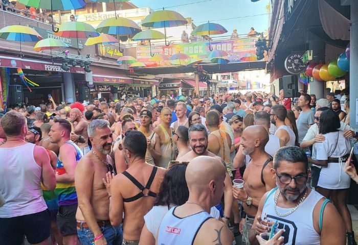 Crowd at Bar Junior, a gay bar in Gran Canaria. Rainbow umbrellas decorate the street. Gay travel destination.