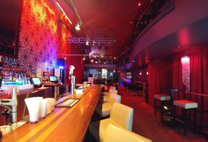 Montreal gay party at Le Cocktail Bar. Features a long bar, red lighting, and a vibrant atmosphere. Great spot for gay men's travel in Montreal.