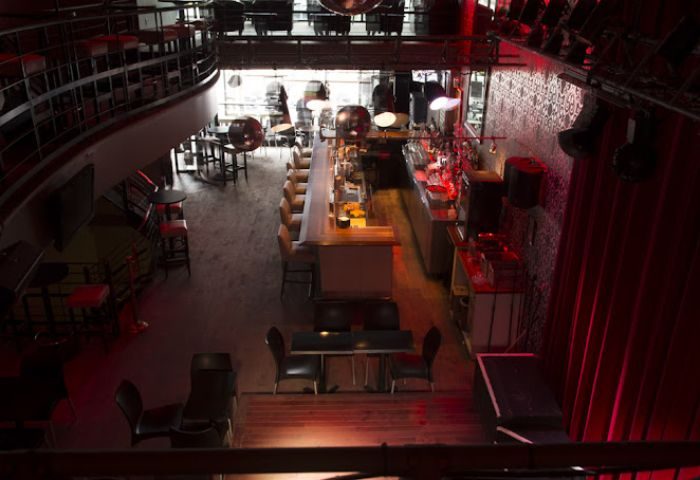Interior of Bar Le Cocktail, a gay bar in Montreal. Two-story venue with bar, stage, and tables. Red lighting. Gay party spot.