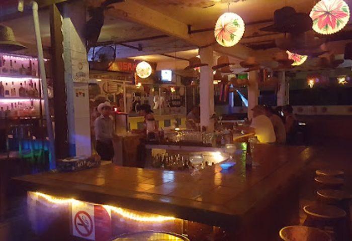 Interior of Los Amigos gay bar in Puerto Vallarta. Bartenders, patrons, and festive decor create a lively atmosphere. Gay travel destination.