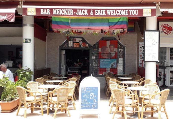 Bar Meicker, a gay bar in Gran Canaria. Outdoor seating, rainbow flag, and a welcoming sign. A popular spot for gay men's travel in the area.