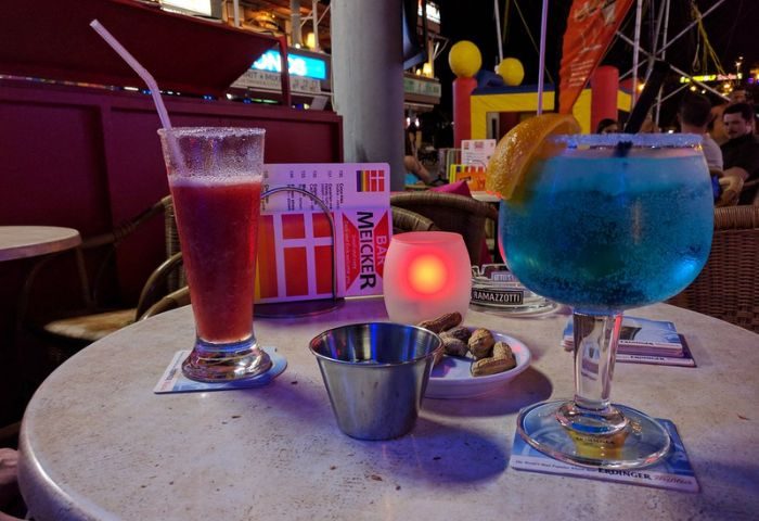 Cocktails at Bar Meicker, a gay bar in Gran Canaria. A red and a blue cocktail sit on a table, peanuts and a candle are also visible.