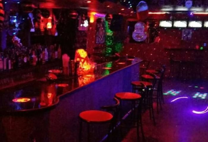 Inside the Mercury gay bar in Benidorm. Red bar stools line the counter, with colorful lights creating a party atmosphere.