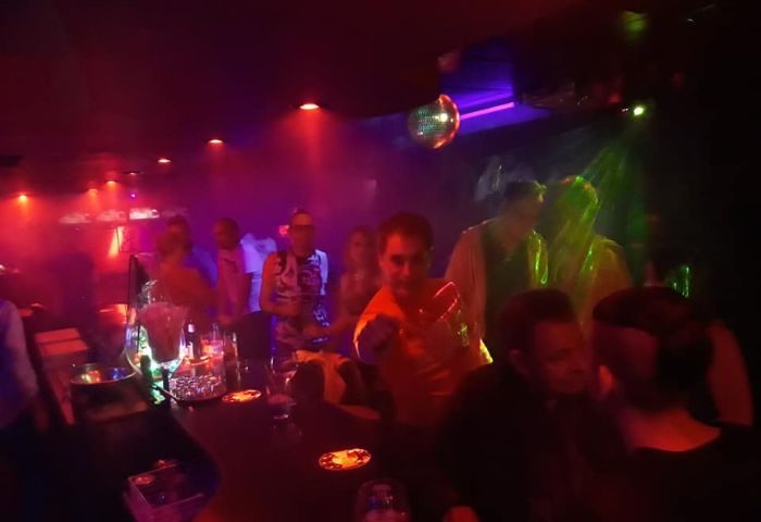 Gay party at Mercury Bar in Benidorm. People enjoy drinks and dance under colorful lights and a disco ball. Gay nightlife scene.