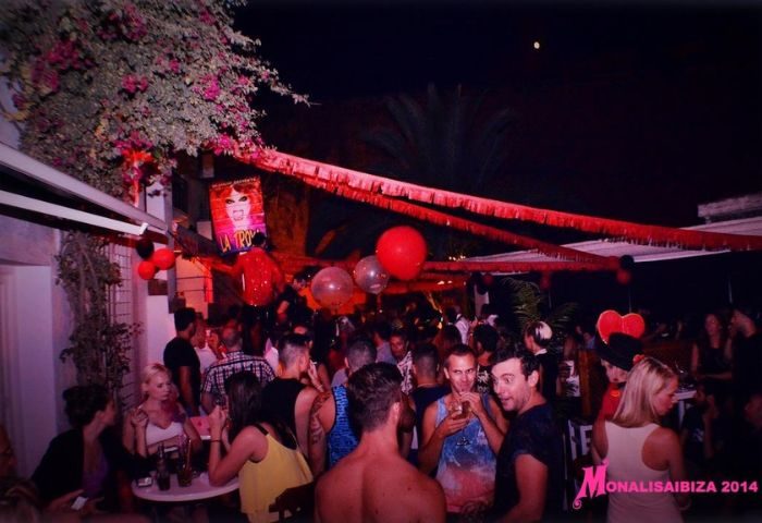 Gay Bar Monalisa Ibiza: Night scene with a crowd of people, red decorations, balloons, and a poster. A lively spot for gay men's travel.