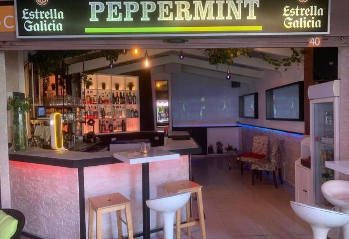 Peppermint Gay Bar in Gran Canaria. Interior view of the bar with stools, tables, and a well-stocked bar. Estrella Galicia sign.