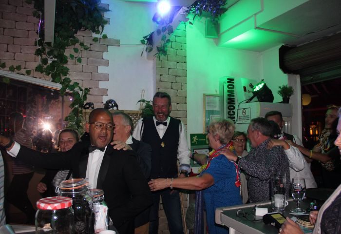 Peppermint Gay Bar in Gran Canaria: Festive scene with men in tuxedos and partygoers, green lighting, lively atmosphere. Gay travel.