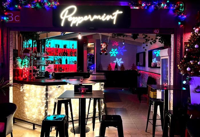 Interior of Peppermint Gay Bar in Gran Canaria, featuring festive decor, bar with colorful lighting, tables, and stools. Gay travel.