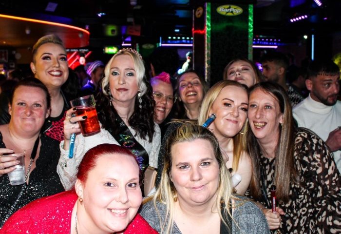 Group of women smiling at Bar Pop Manchester, a gay bar. Nightlife scene with drinks and neon lights. Gay travel destination.
