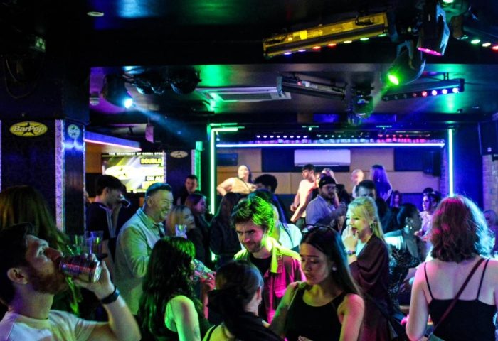 Inside Bar Pop Manchester, a lively gay bar. Patrons are enjoying drinks and socializing under colorful club lighting. Gay travel advice.