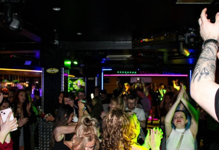 Manchester's Bar Pop scene: A vibrant crowd enjoying a night out at a gay bar, dancing under colorful lights. Gay travel advice.