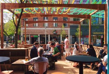 Outdoor patio at Bar Renard in Montreal. People sit at tables, enjoying drinks. Gay travel destination with a lively atmosphere. Summer in Canada.