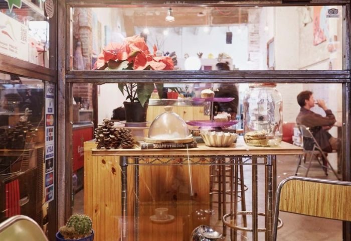 Barcelona's Bar Rufián gay bar interior. View through the window: cupcakes, plants, and a man seated at a table. Stylish, inviting.