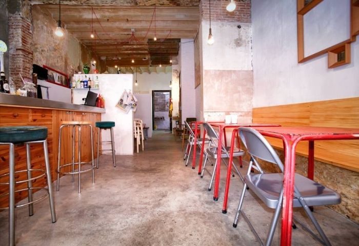 Interior of Bar Rufián, a gay bar in Barcelona. Rustic design with exposed brick, red tables, and bar seating. A cool spot for gay men.