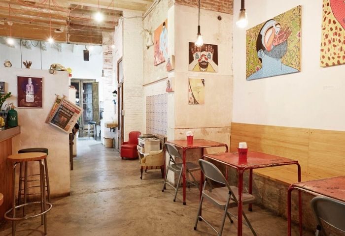 Interior of Bar Rufián, a gay bar in Barcelona. Tables, chairs, and artwork adorn the rustic space, creating a welcoming atmosphere.