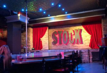 Interior of Stock Bar in Montreal, a gay stripper liveshow venue. Stage with red curtains, pole, and bar seating. Nightlife spot.