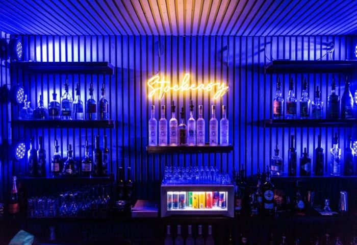 Montreal gay bar stock. Blue-lit bar shelves stocked with liquor bottles. Stockeasy neon sign. Gay stripper liveshow venue. Travel advice.